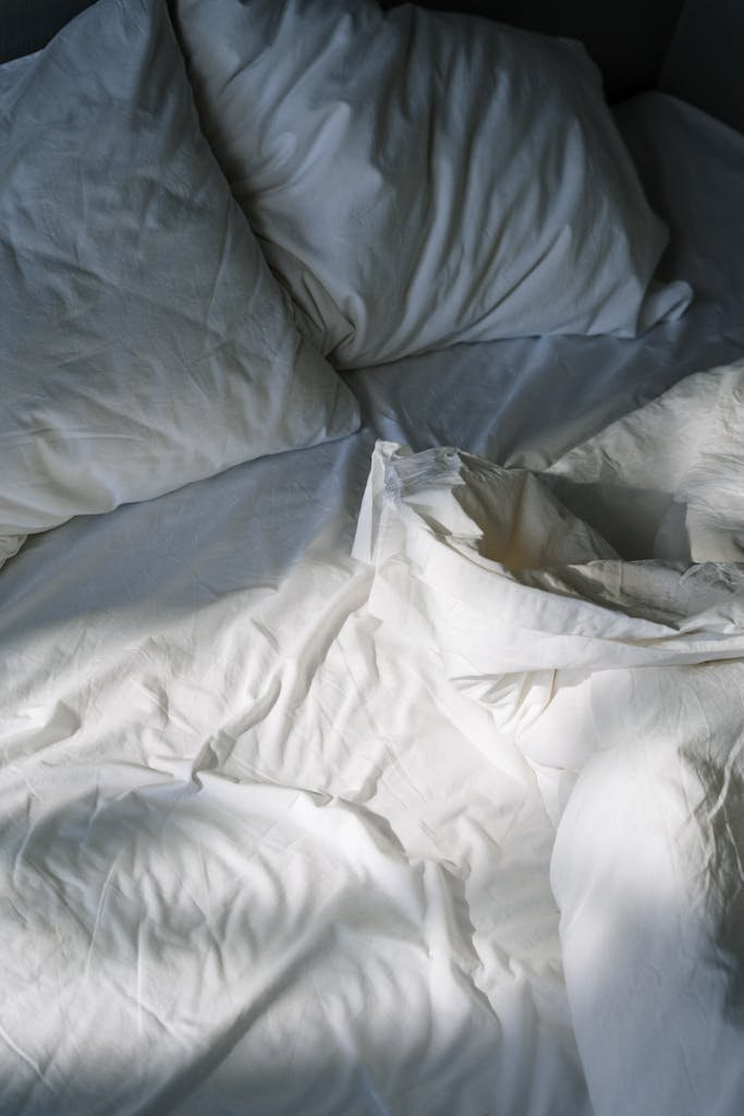 A cozy, inviting bed with white linens lit by morning sunlight, creating a restful atmosphere.
